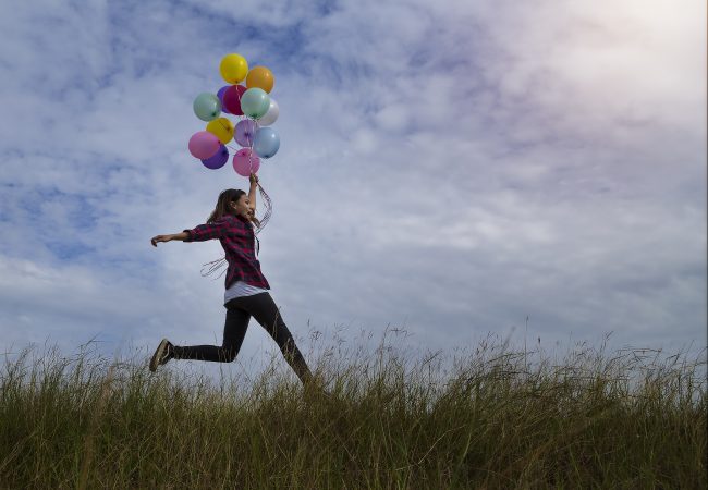 Beautiful girl holding balloons running in prairie grass. On a clear day
